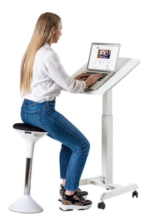 kvinna sitter på en balanspall framför ett litet höj och sänkbart skrivbord på hjul.